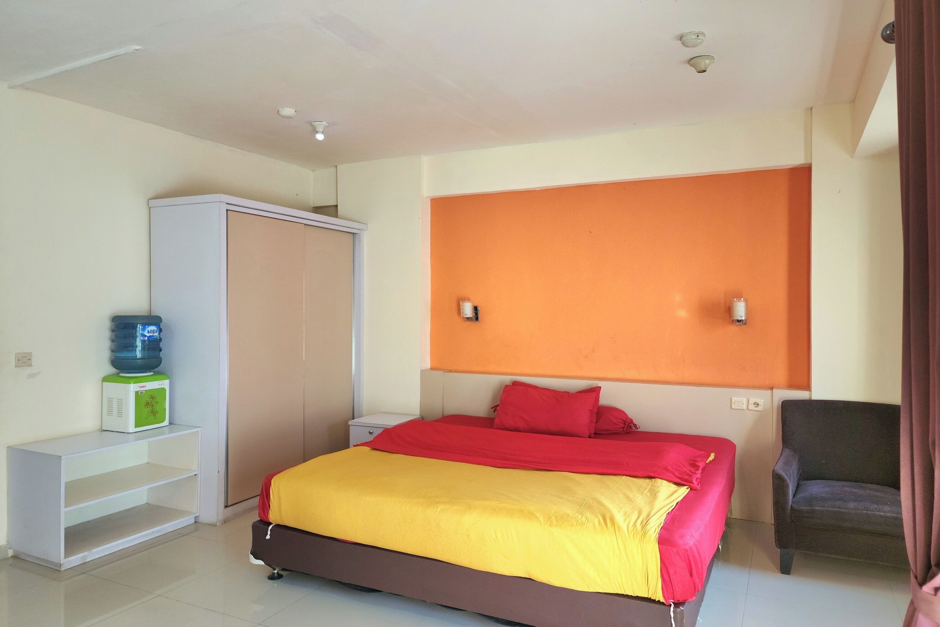Une chambre à coucher comprenant un lit, une armoire, un distributeur d’eau, une chaise et une table de chevet.