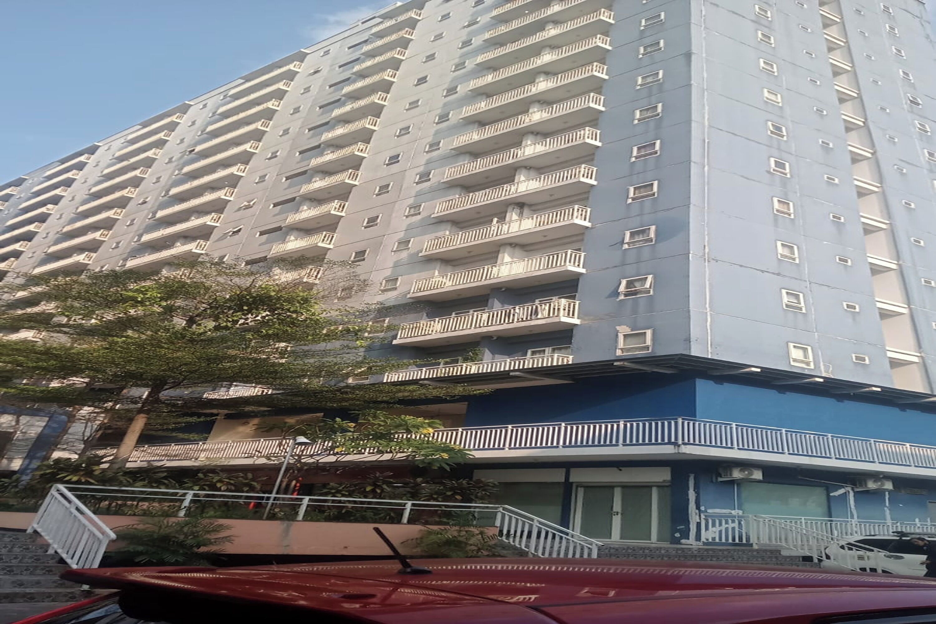 A multi-story residential building with balconies, a gated entrance, and a parked car.