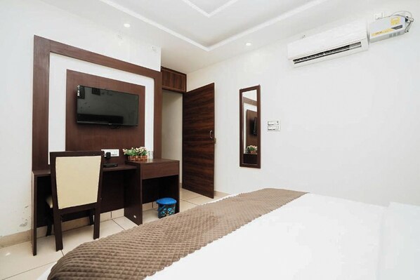 A bedroom with a bed, a desk with a chair, a television, and a wardrobe.