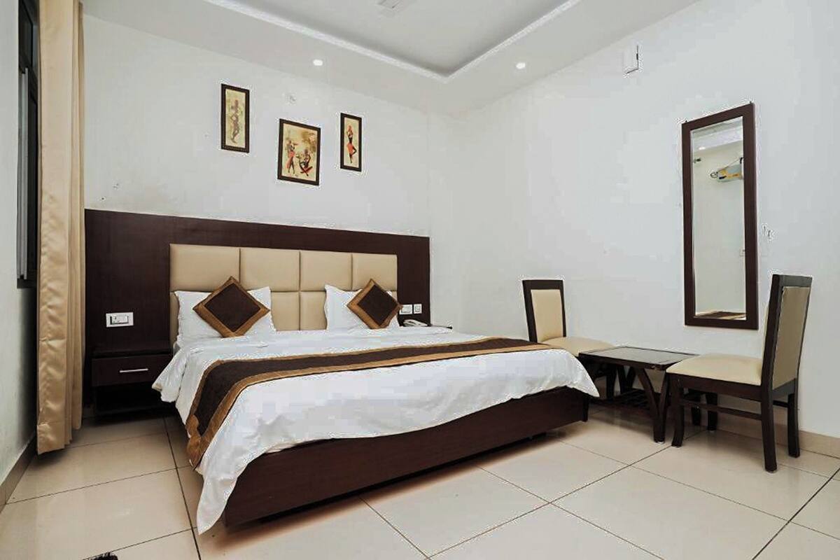 A hotel room with a large bed, a desk, and chairs. There are framed pictures on the wall and a mirror.