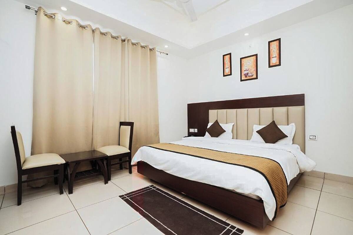 A hotel room with a large bed, two chairs, a small table, and a view of the city.
