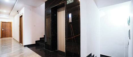 A modern hallway with a marble floor, a black elevator, and a wooden door at the end.