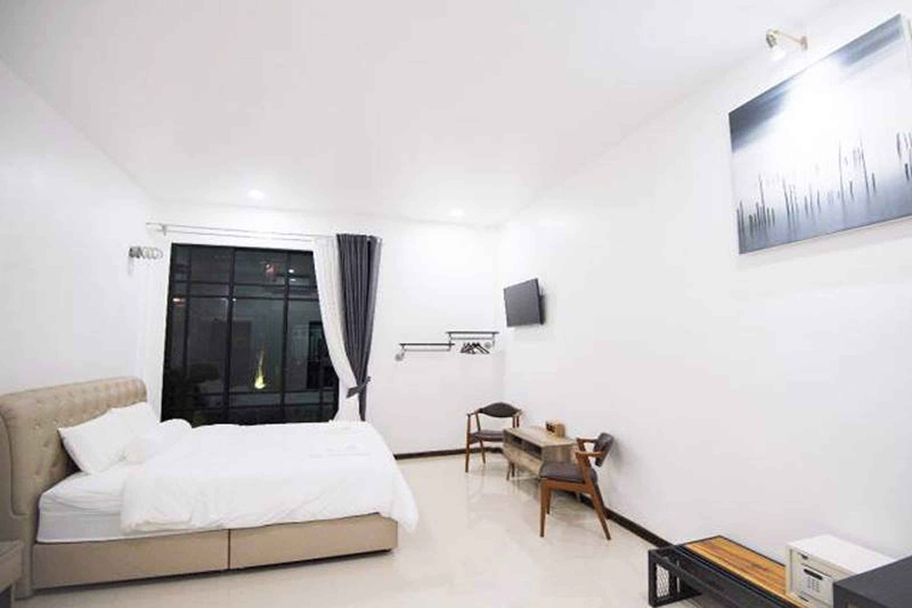 Moderni hotellihuone, jossa on sänky, työpöytä, tuoli, televisio ja ikkuna, jossa on verhot.