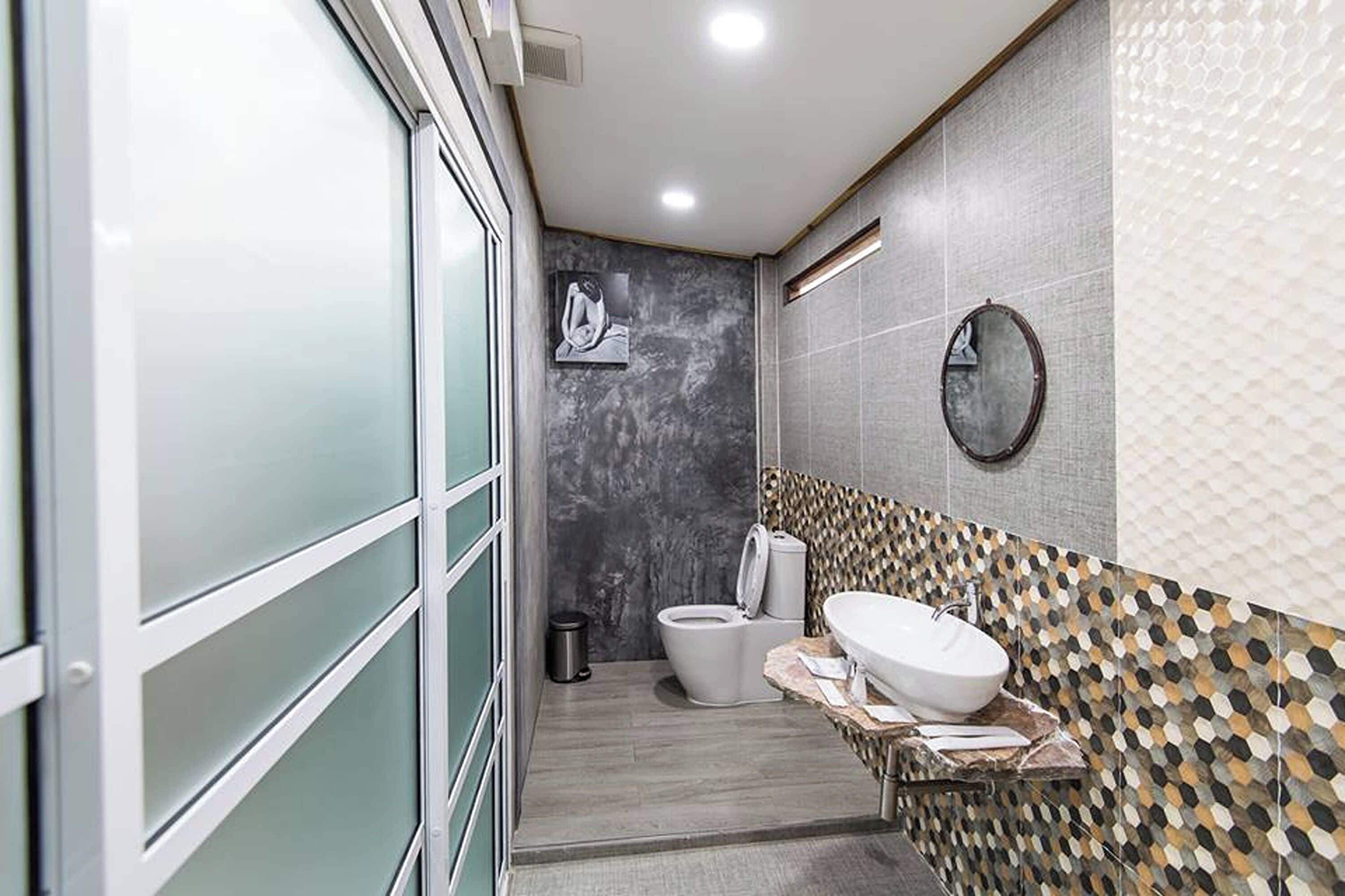A modern bathroom with a glass shower enclosure, a toilet, and a sink with a decorative mirror.