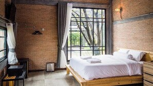 Une chambre avec une grande fenêtre, un lit, un luminaire suspendu et un mur en briques.