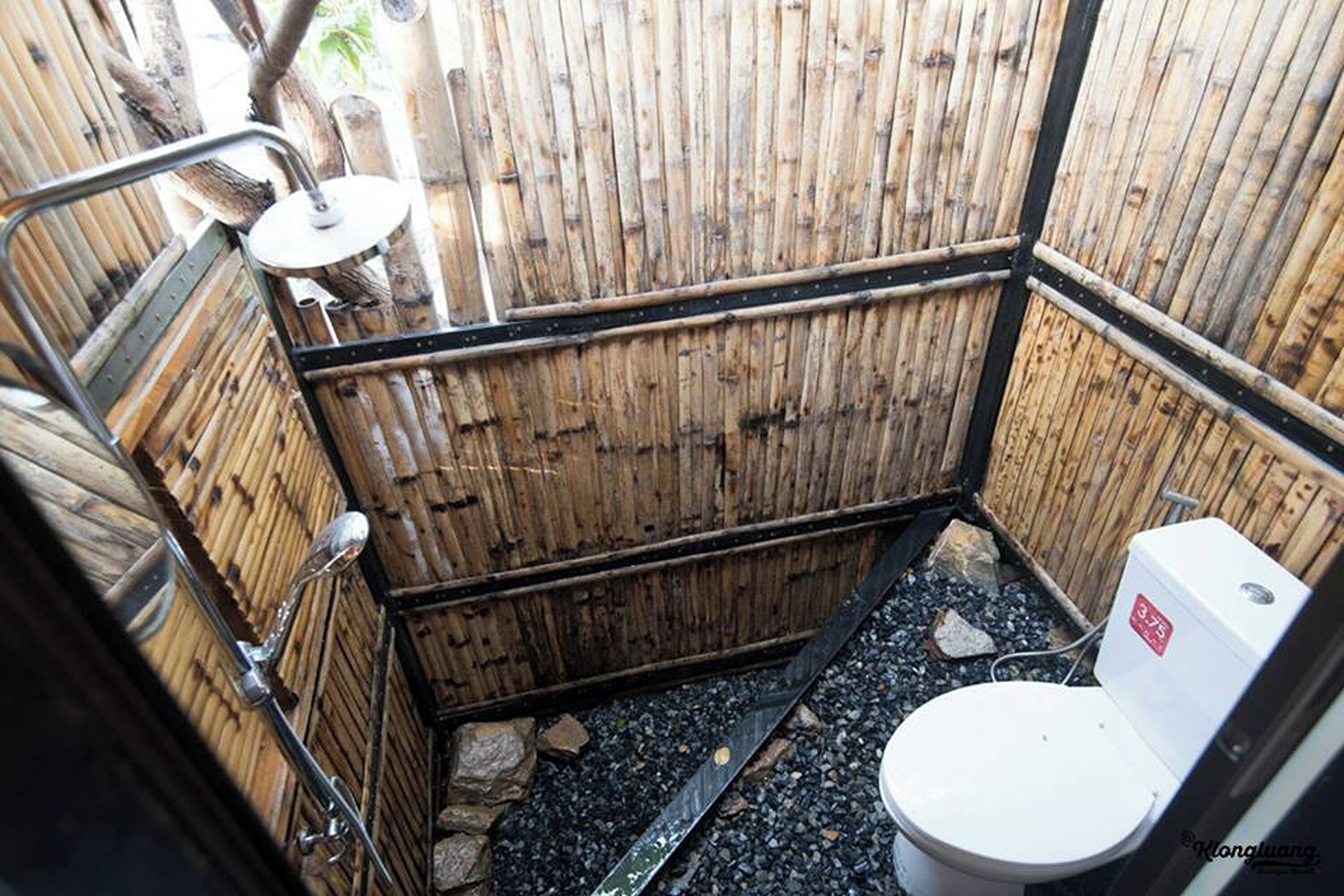 Ein kleines, rustikales Badezimmer mit Bambuswand, einer weißen Toilette und einer Duschkabine aus Metall.