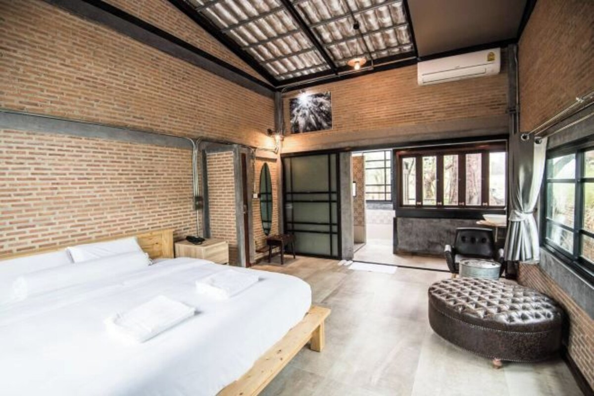 Une chambre d’hôtel moderne avec un grand lit, un banc en bois et un pouf rond.