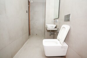 A modern bathroom with a white toilet, a sink, and a mirror. - Hotel Elegance Nx (Mumbai)
