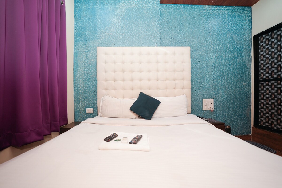 A neatly made bed with a white headboard, a purple curtain, and a remote control on the bed.