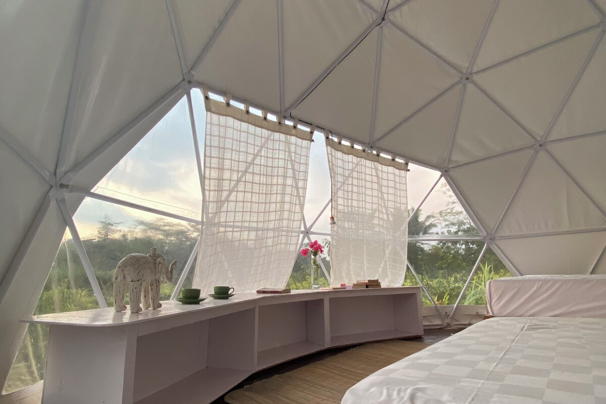 Een tentaccomodatie met een bed, een zithoek met uitzicht en een decoratief olifantbeeld.