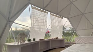 Un hébergement sous tente comprenant un lit, une étagère avec des objets décoratifs et une vue sur l’extérieur.