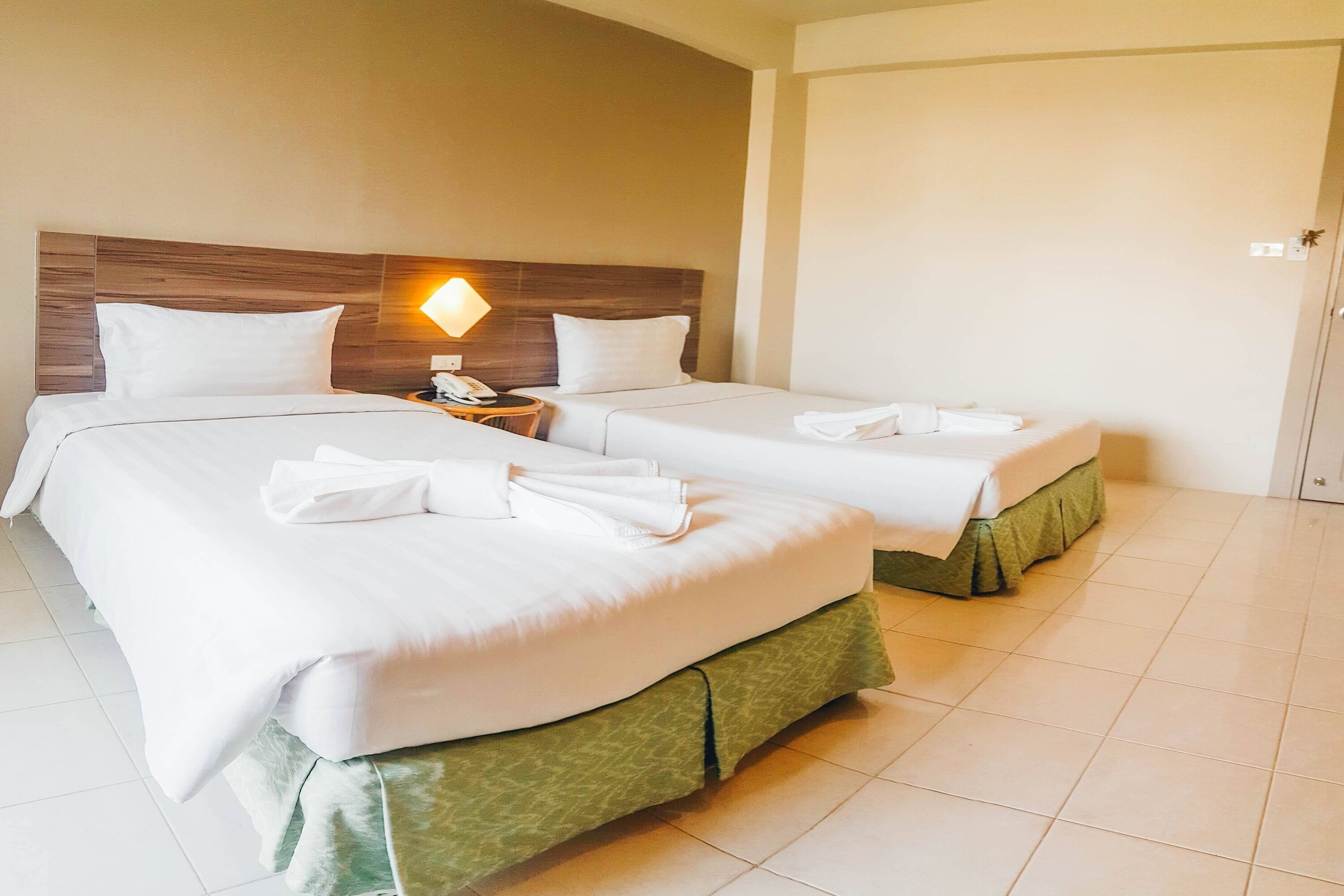 Habitación de hotel con dos camas, una mesita de noche con lámpara y una puerta con picaporte.