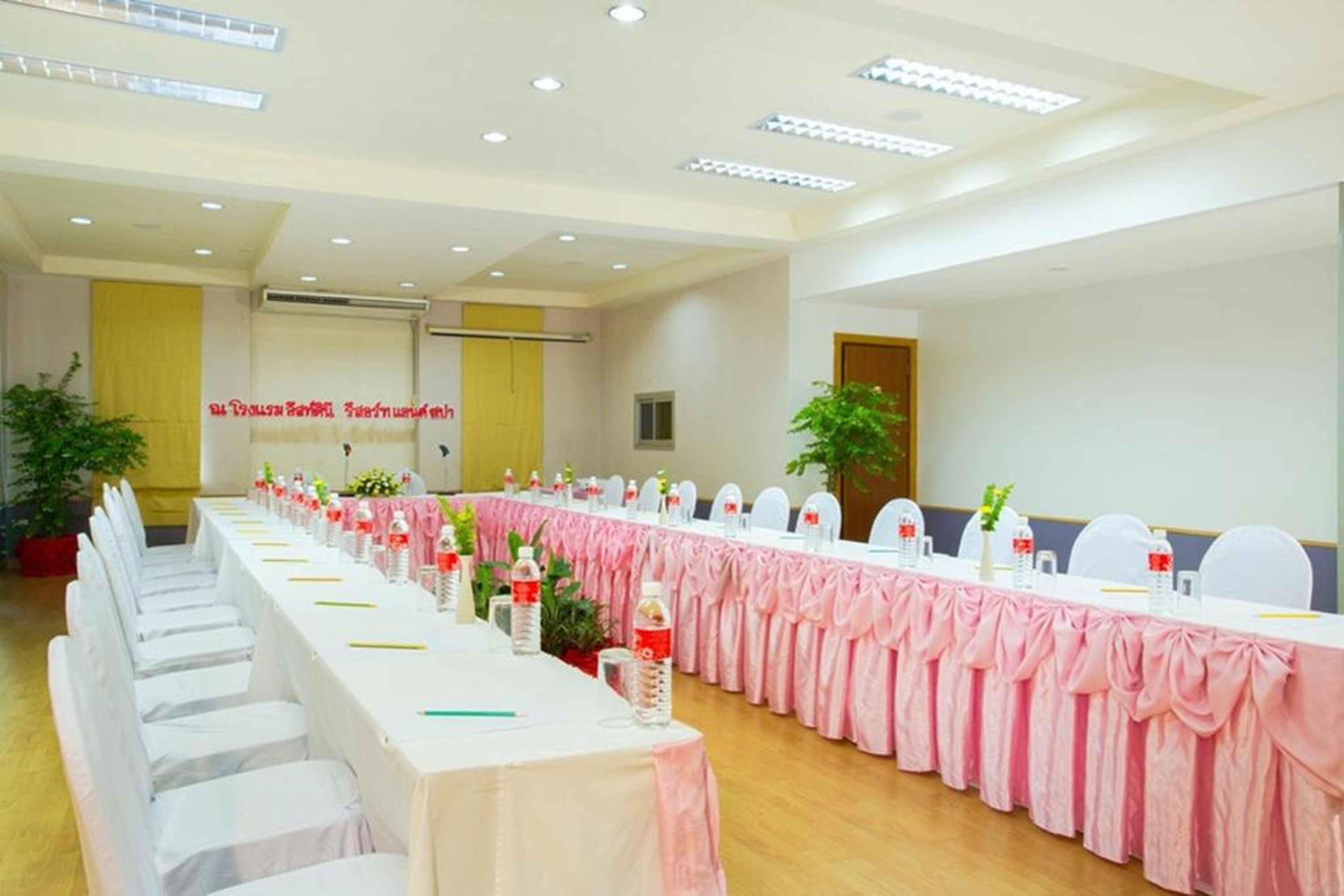 A conference room with a long table, white chairs, and a pink tablecloth.