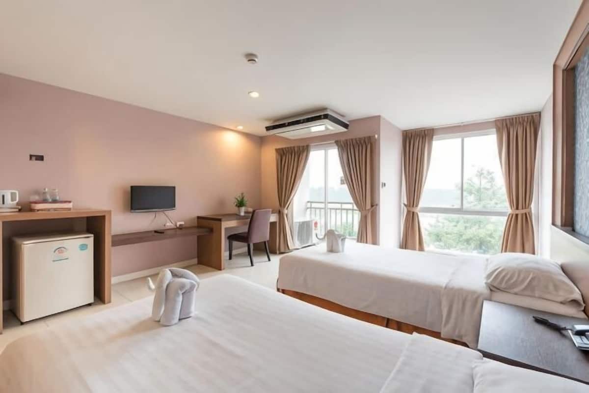 A hotel room with two beds, a desk, a TV, and a balcony with curtains.