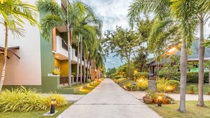 A pathway flanked by palm trees and potted plants, leading to a building with balconies. - Eastiny Resort & Spa (Pattaya)