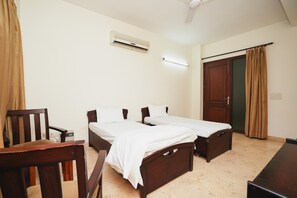 A room with two wooden beds, a desk, a chair, an air conditioning unit, and a door. - Home 92 (Noida)