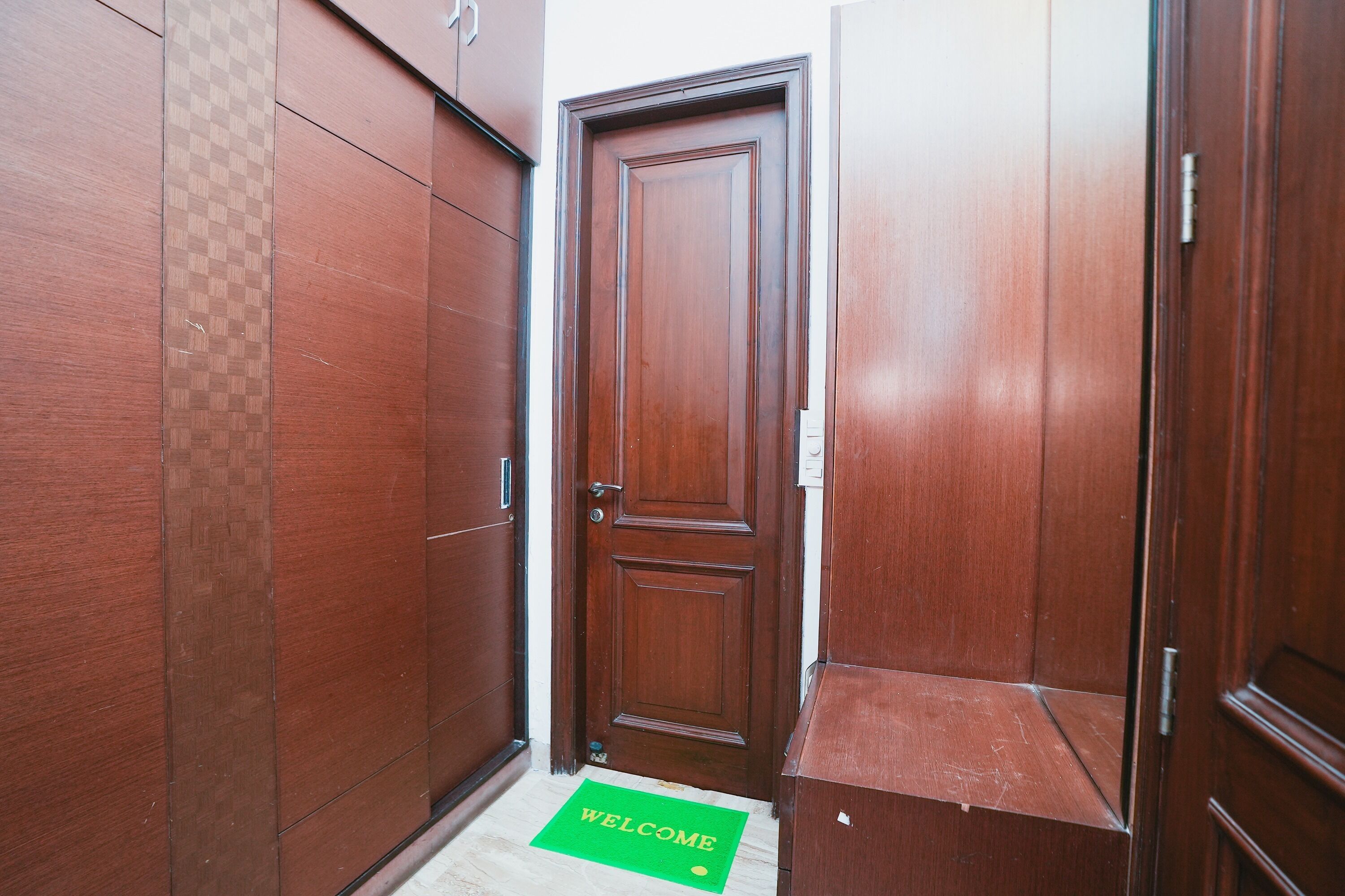 A narrow hallway with wooden doors and a green welcome mat.