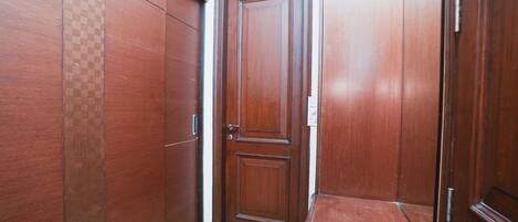 A narrow hallway with wooden doors and a green welcome mat.