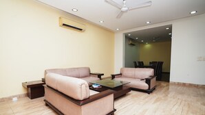 A living room with two beige sofas, a glass coffee table, and a ceiling fan. - Home 92 (Noida)
