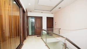 A hallway with a glass railing, wooden doors, and a light-colored floor. - Home 92 (Noida)