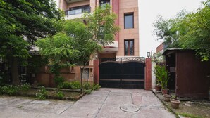 A gated entrance to a residential building with a paved driveway, a manhole cover, and potted plants along the pathway. - Home 92 (Noida)