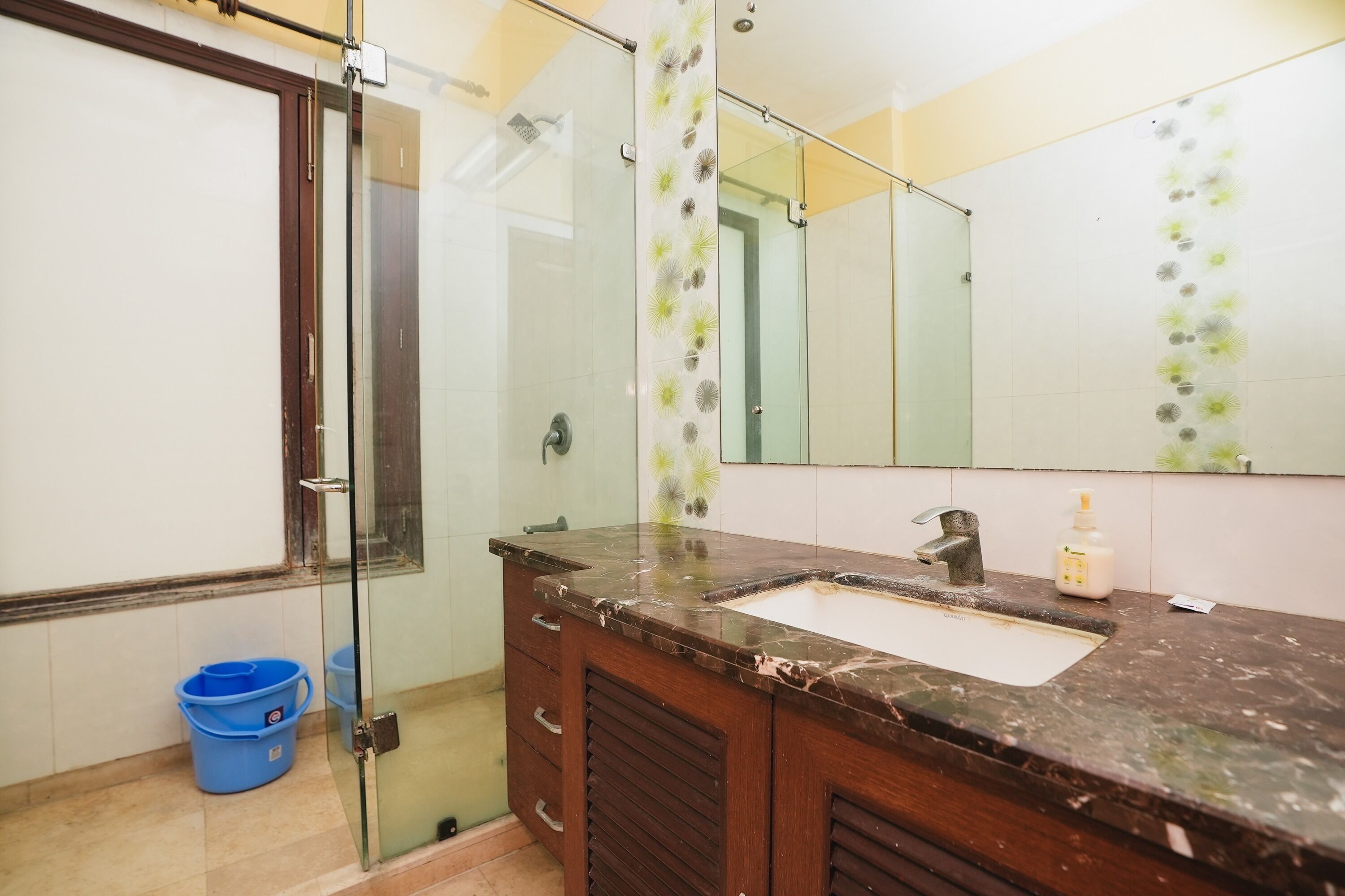 A bathroom with a glass shower enclosure, a sink with a marble countertop, and a large mirror.