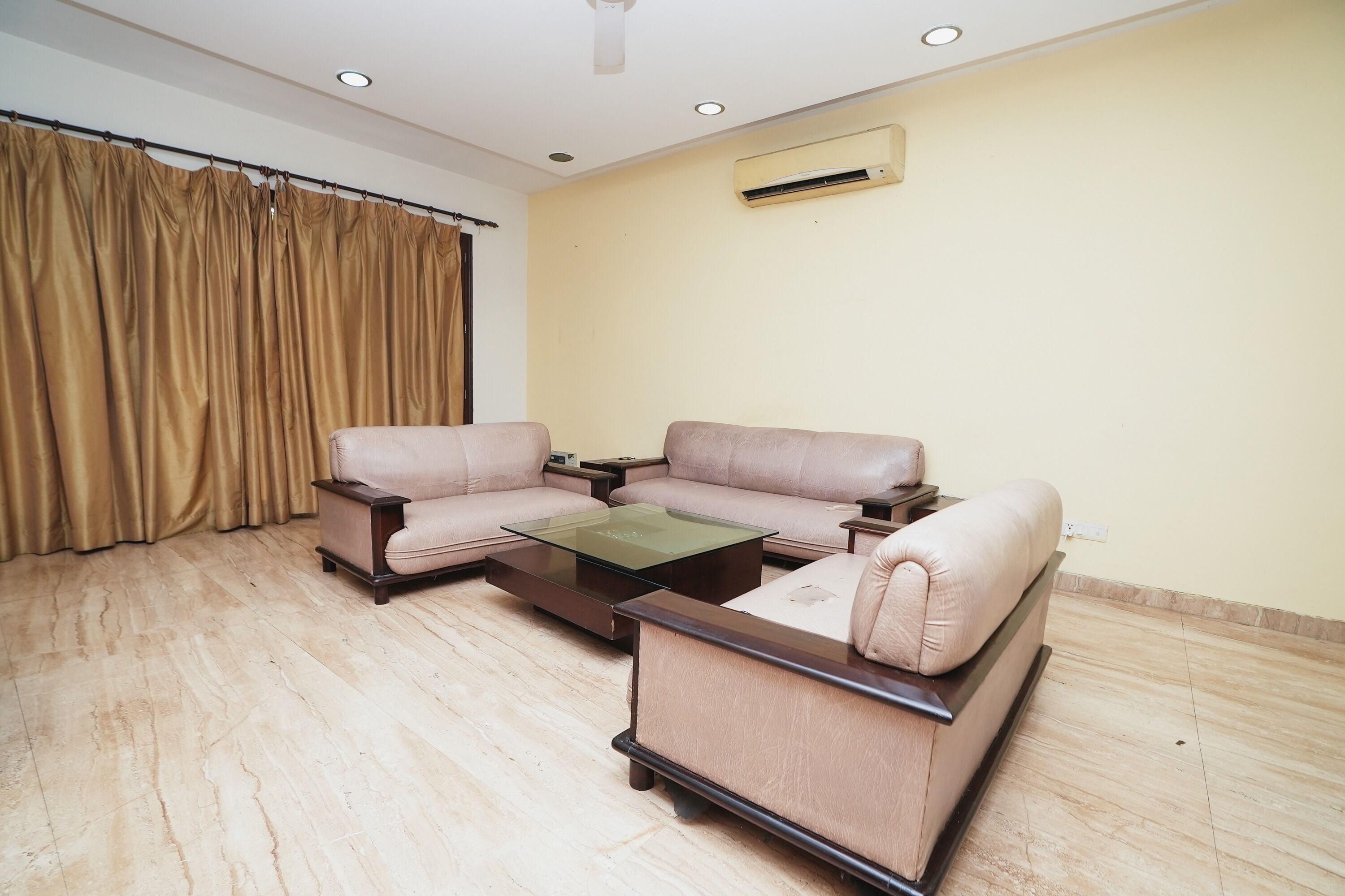 A living room with a beige sofa set, a glass coffee table, and a beige armchair.