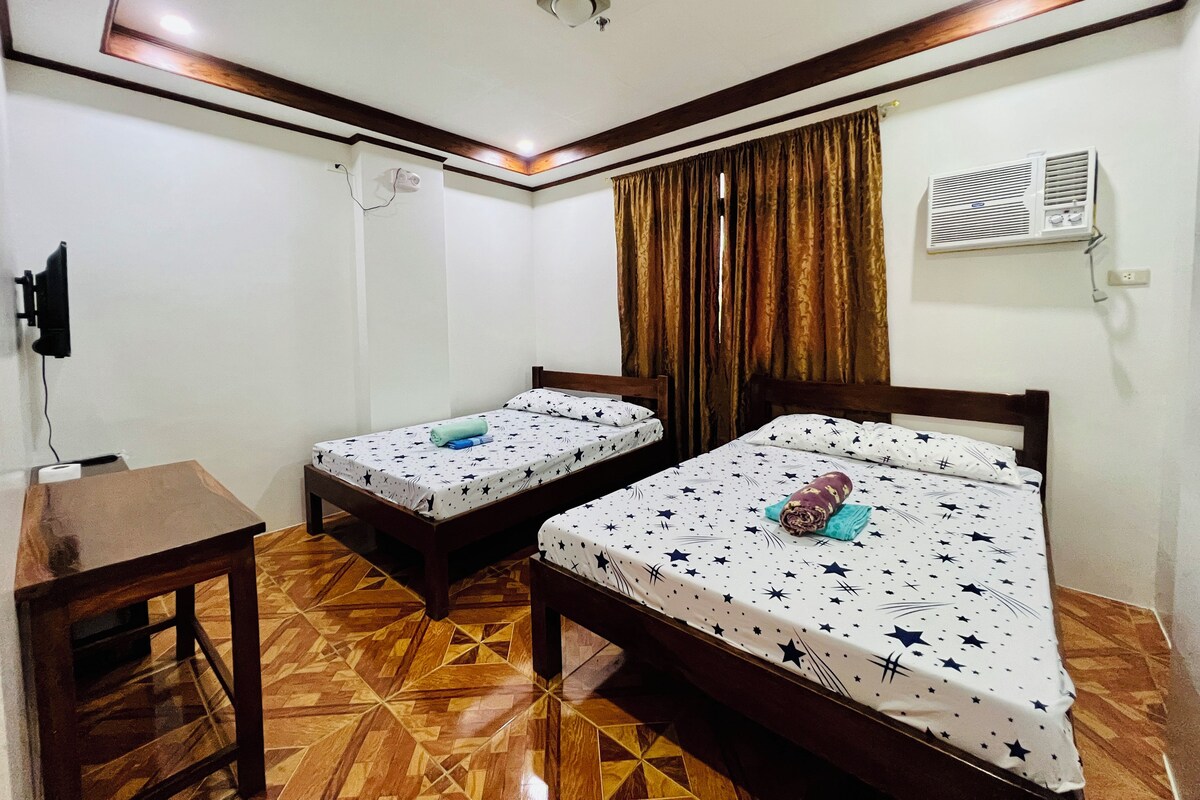 A room with two beds, a wooden table, and an air conditioning unit.