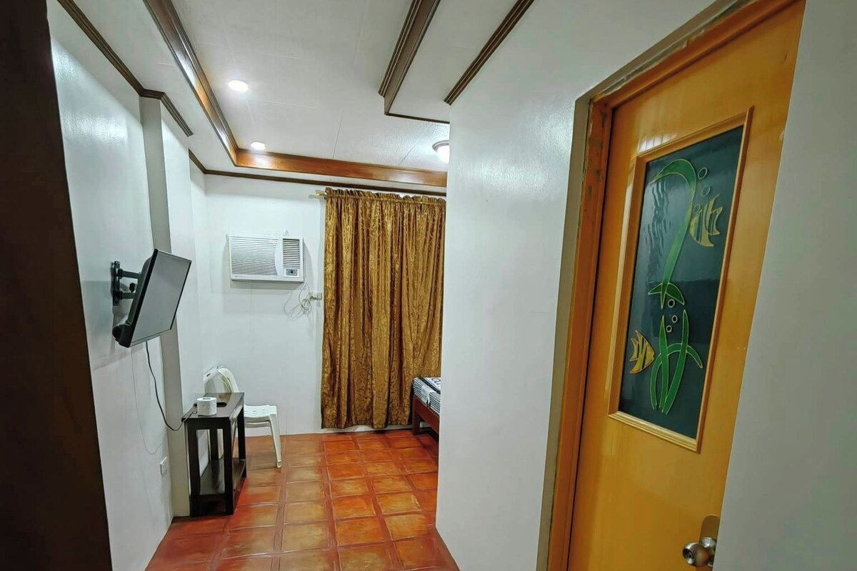 A hallway with a tiled floor, a white wall with an air conditioning unit, a white chair, and a door with a green abstract painting.