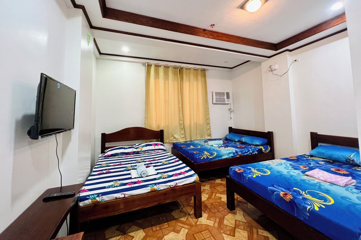 A room with two beds, a TV mounted on the wall, and an air conditioning unit.