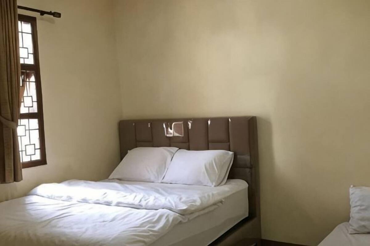 A single bed with a headboard, a window with a curtain, and a plain wall.
