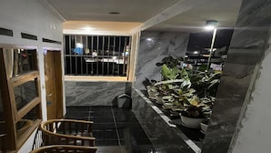 A narrow hallway with black tiled flooring, wooden chairs, and a row of potted plants against the wall. - Villa Buana Graha Syariah (Lembang)