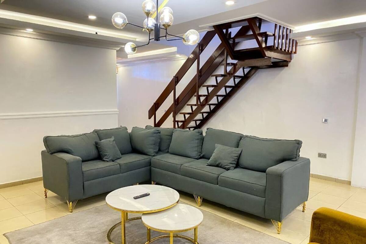 A modern living room with a sectional sofa, two round coffee tables, a staircase, and a yellow armchair.