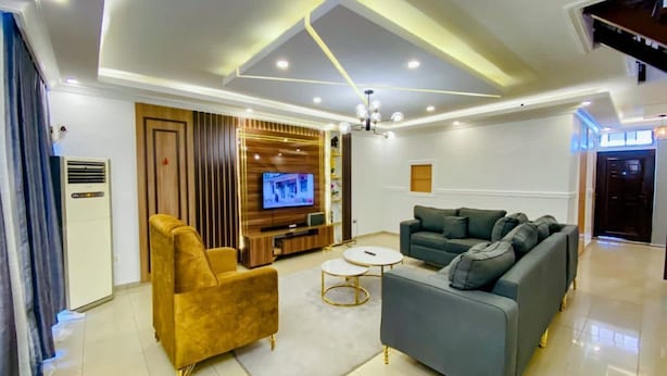 A modern living room with a sofa, armchair, and entertainment unit. - Deluxe Apartment (Lagos)
