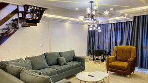 A modern living room with a sectional sofa, a round coffee table, a yellow armchair, and a staircase. - Deluxe Apartment (Lagos)