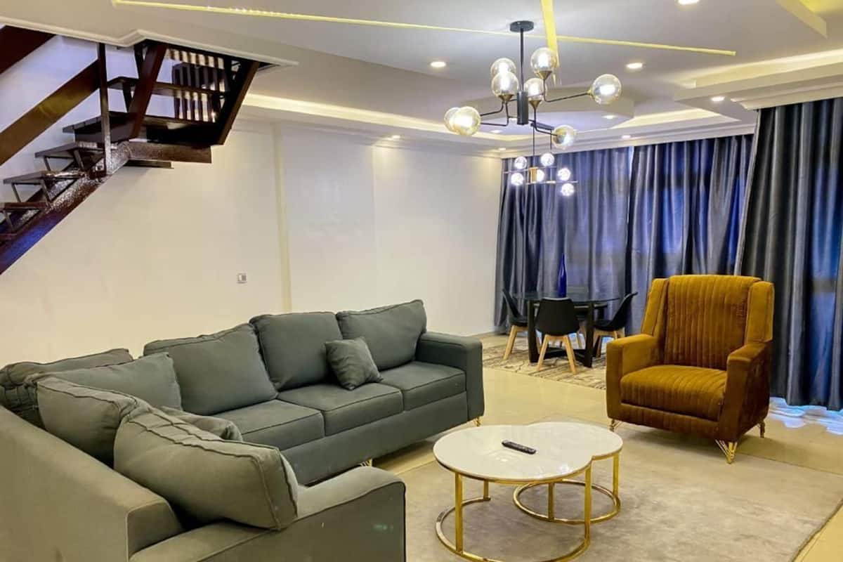 A modern living room with a sectional sofa, a round coffee table, a yellow armchair, and a staircase.