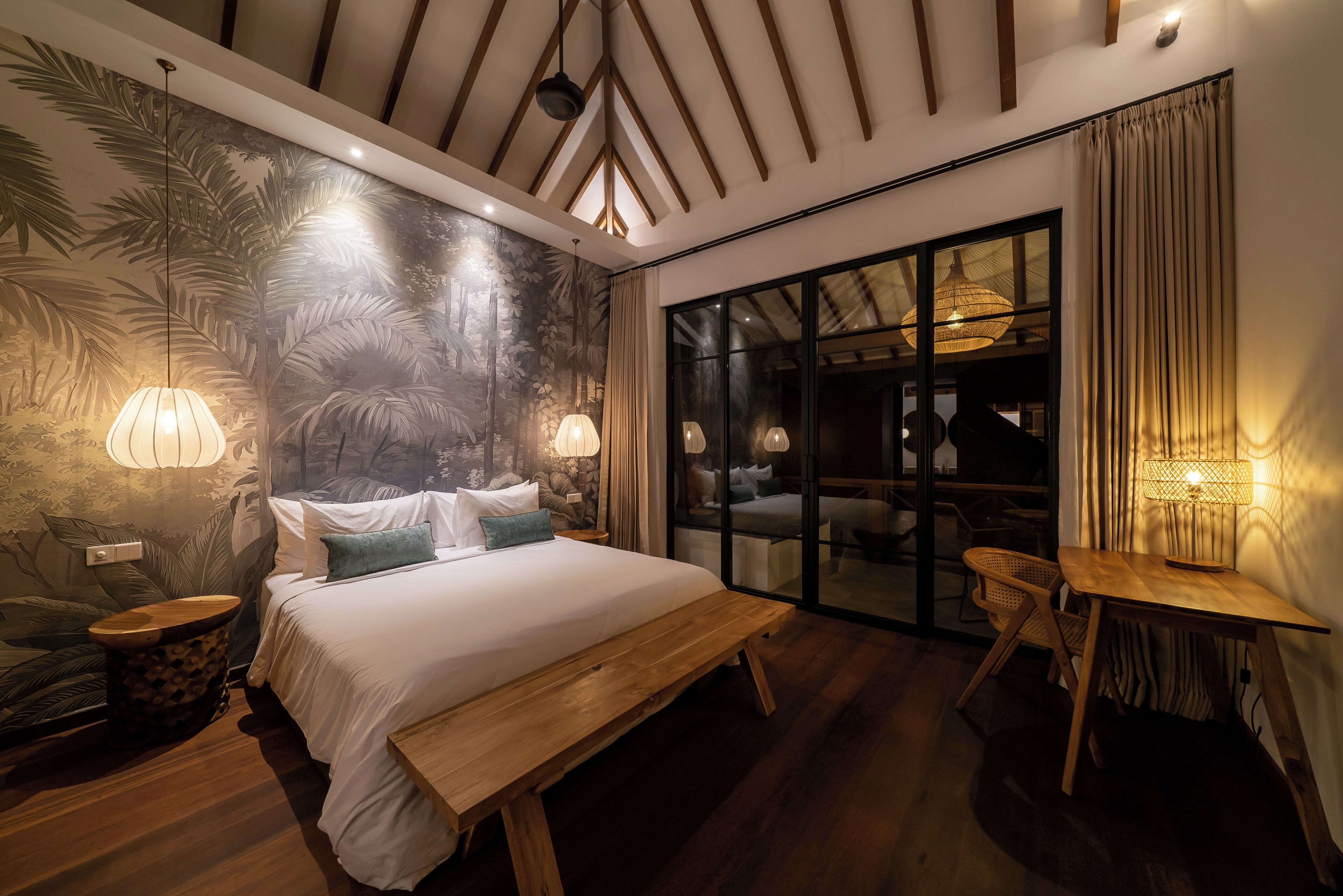 A bedroom with a large bed, wooden bench, and a view through a glass door.