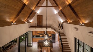A spacious interior with a high ceiling, wooden beams, a central chandelier, a staircase, and a kitchen area. - Villa Nusantara 5 by Alfred in Bali (Canggu)