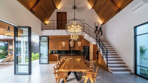 A spacious dining area with a large wooden table and chairs, a chandelier, and a staircase leading to an upper level. - Villa Nusantara 5 by Alfred in Bali (Canggu)