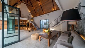A spacious living area with a high ceiling, a staircase, a dining area, and a large window. - Villa Nusantara 5 by Alfred in Bali (Canggu)