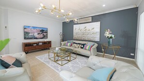 A modern living room with a beige sofa, a glass coffee table, and a large flat-screen TV. - Hallam 5BRM Rental Entire House (Hallam)