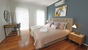 A bedroom with a bed, bedside table, lamp, and a desk with a chair. - Hallam 5BRM Rental Entire House (Hallam)