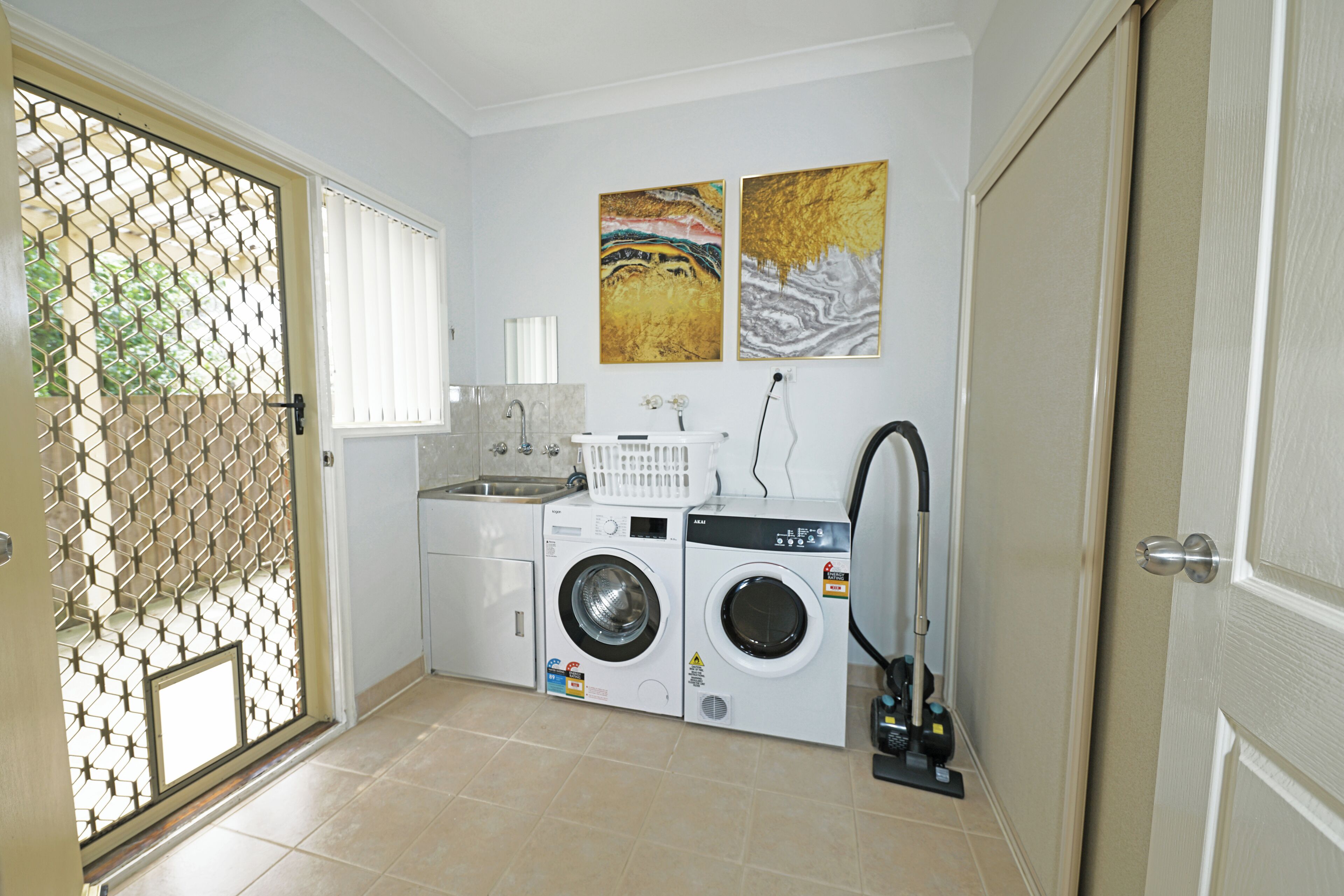A laundry room with two washing machines, a dryer, and a sink.