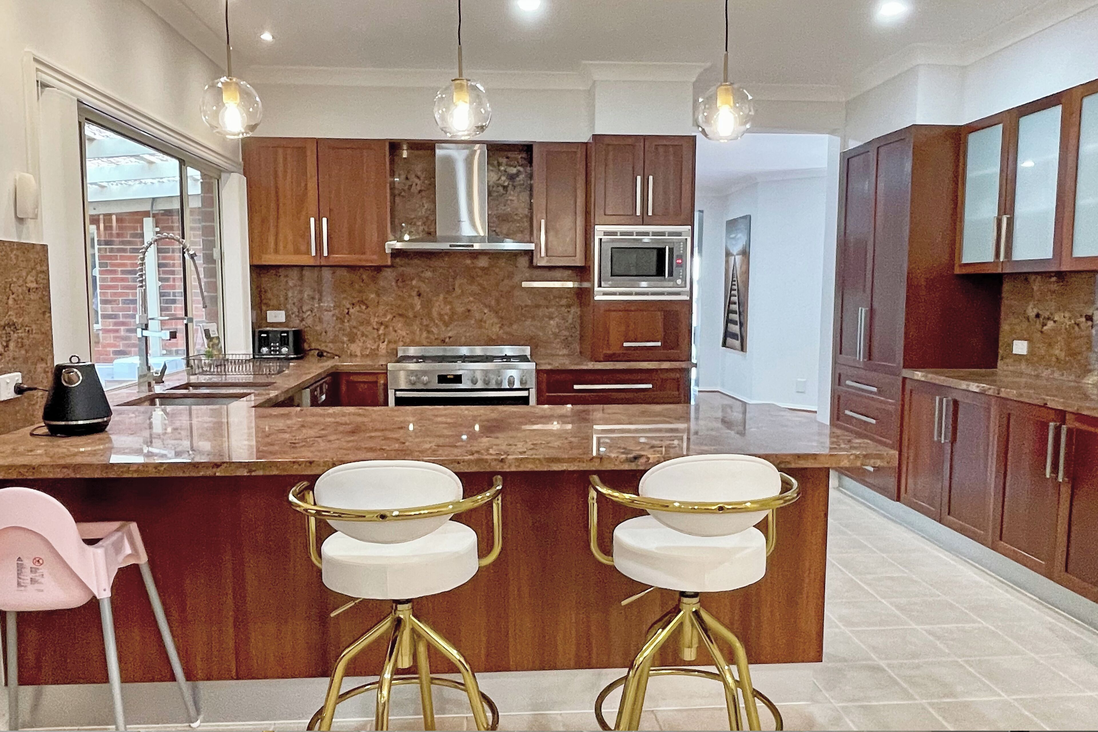 A modern kitchen with a central island, stainless steel appliances, wooden cabinets, and pendant lighting.