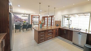 A modern kitchen with a central island, built-in appliances, and a dining area with chairs and a table. - Hallam 5BRM Rental Entire House (Hallam)