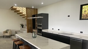 A modern kitchen with a marble countertop, wooden stools, a built-in oven, and a staircase with wooden panels. - Hear the waves from either pools or patios, or walk to the beach, ocean views (Manuel Antonio)