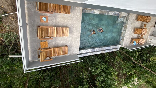 An aerial view of a modern outdoor pool area with wooden seating and a clear blue pool. - Hear the waves from either pools or patios, or walk to the beach, ocean views (Manuel Antonio)