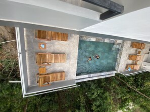An aerial view of a modern outdoor pool area with wooden seating and a clear blue pool. - Hear the waves from either pools or patios, or walk to the beach, ocean views (Manuel Antonio)