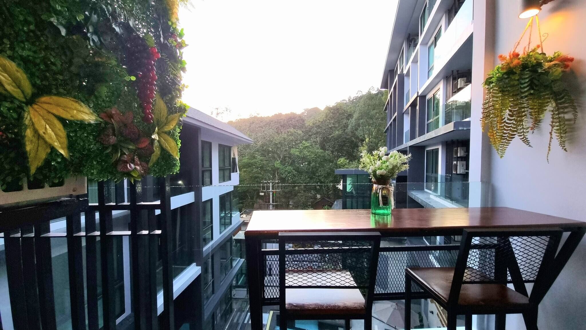 Uma varanda moderna ao ar livre, com mesa e cadeiras de madeira, rodeada por vegetação exuberante e plantas pendentes.