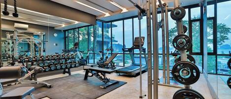 Un gimnasio moderno con diversos equipos de ejercicio, ventanas amplias y vista a la ciudad.